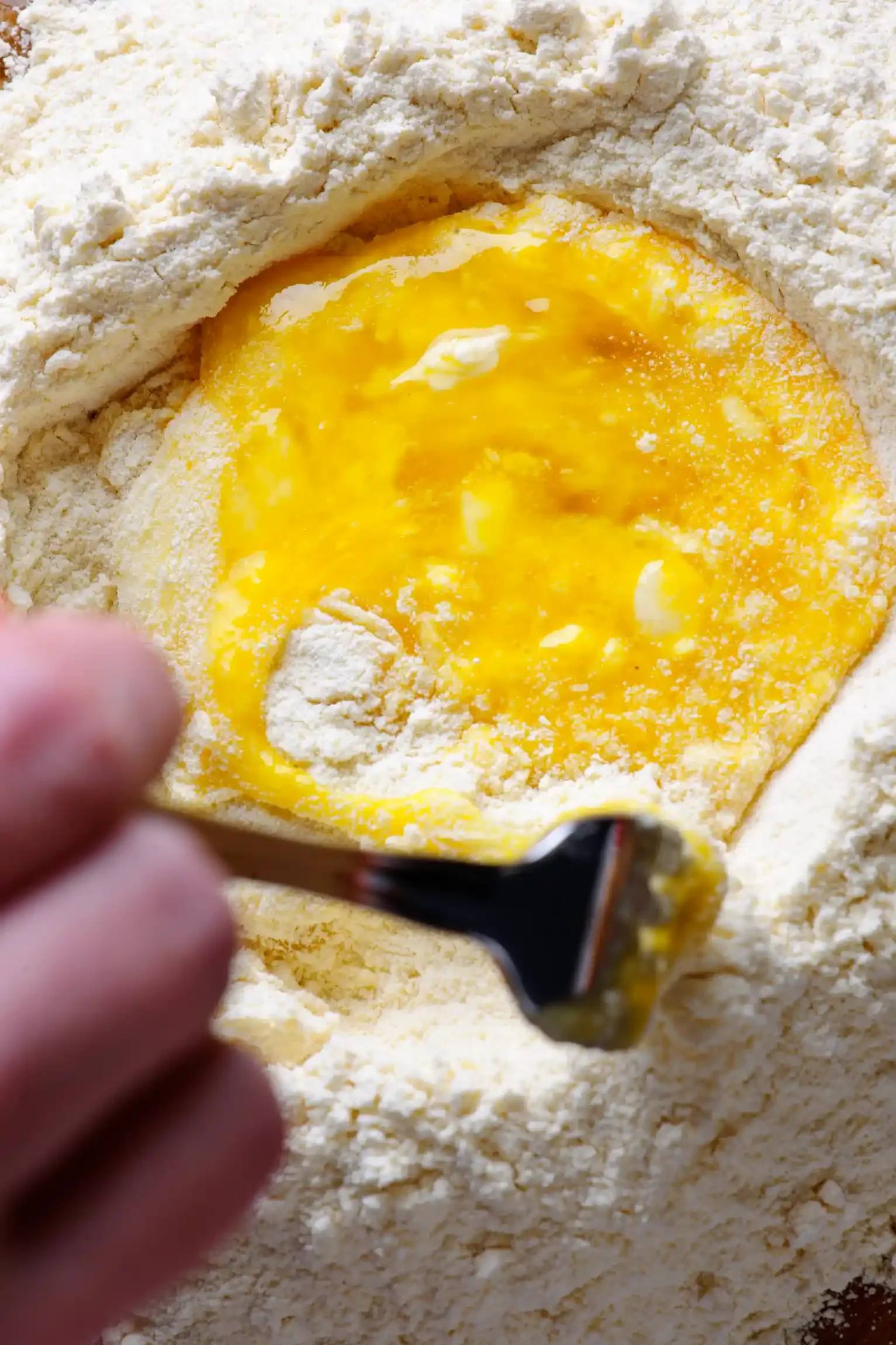 A person mixing eggs into flour for baking, using a spoon in a close-up shot. By Philadelphia, PA & NJ food photographer & food stylist team Bartholomew Studio.