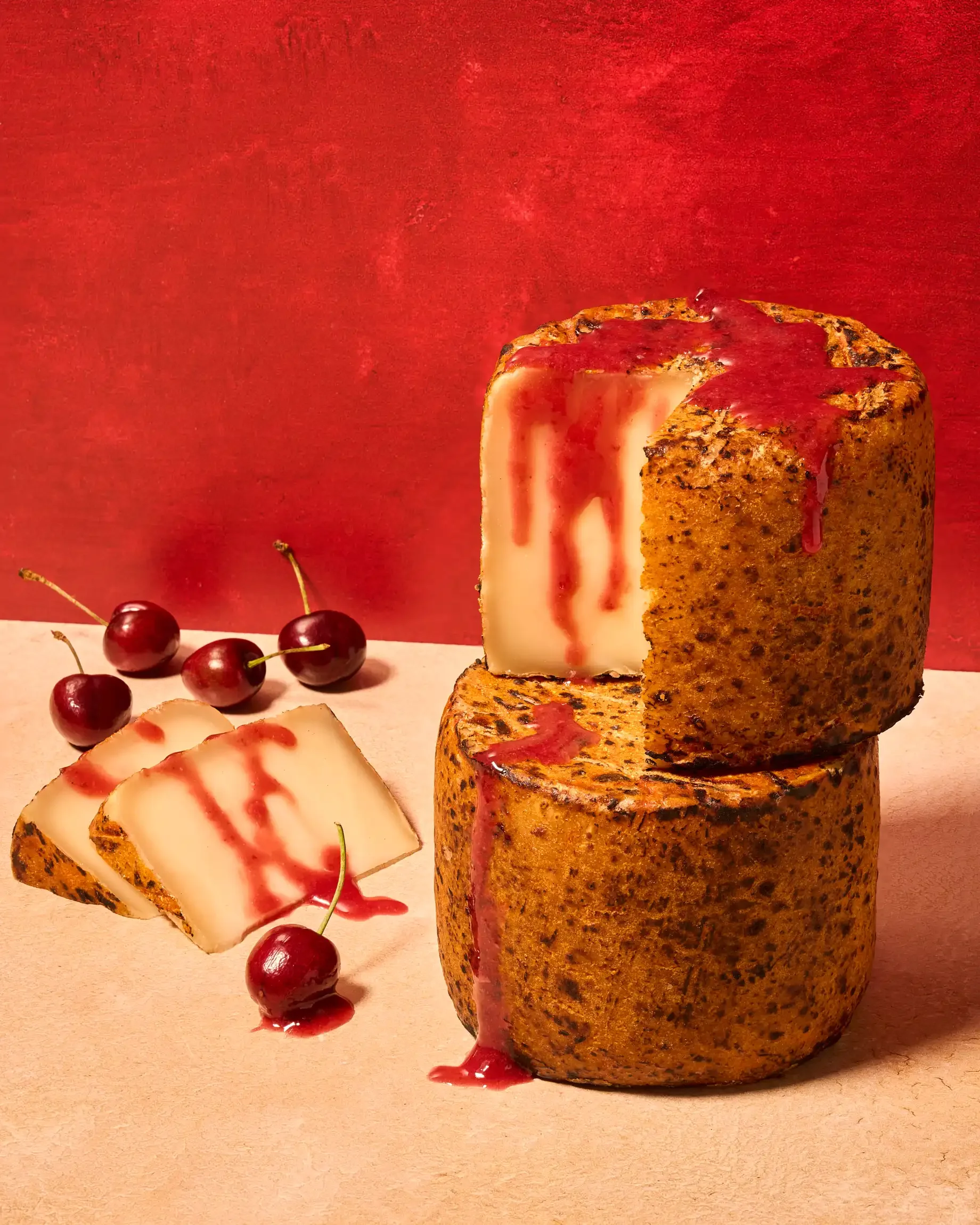 Tomme Brulee cheese with cherry sauce on a beige surface with a red background. Food styling by Andrea Bartholomew