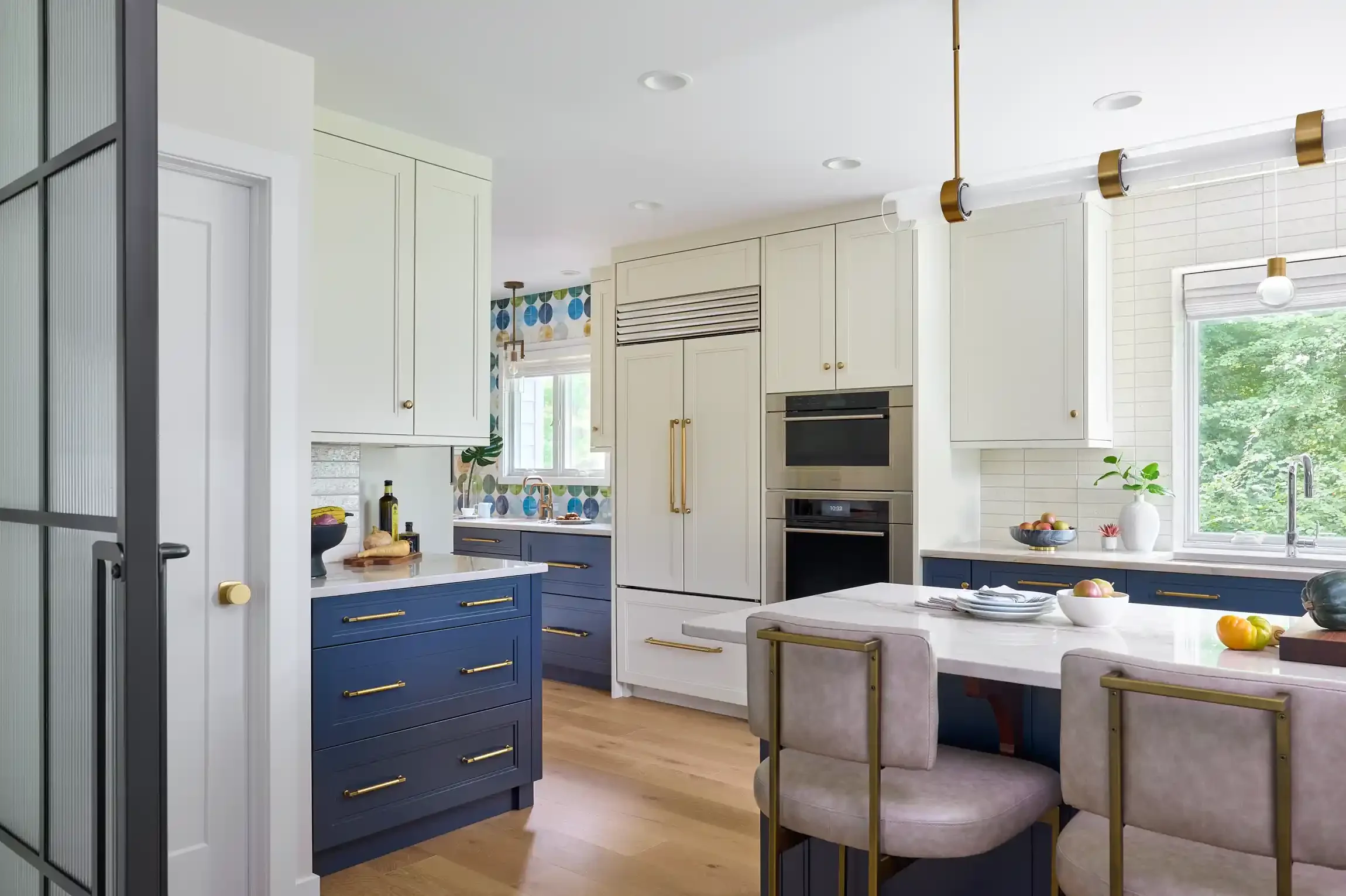 Modern kitchen with white upper cabinets, blue lower cabinets with gold handles, and a white marble island with gold accents. By New Jersey home interior photographer Bartholomew Studio.