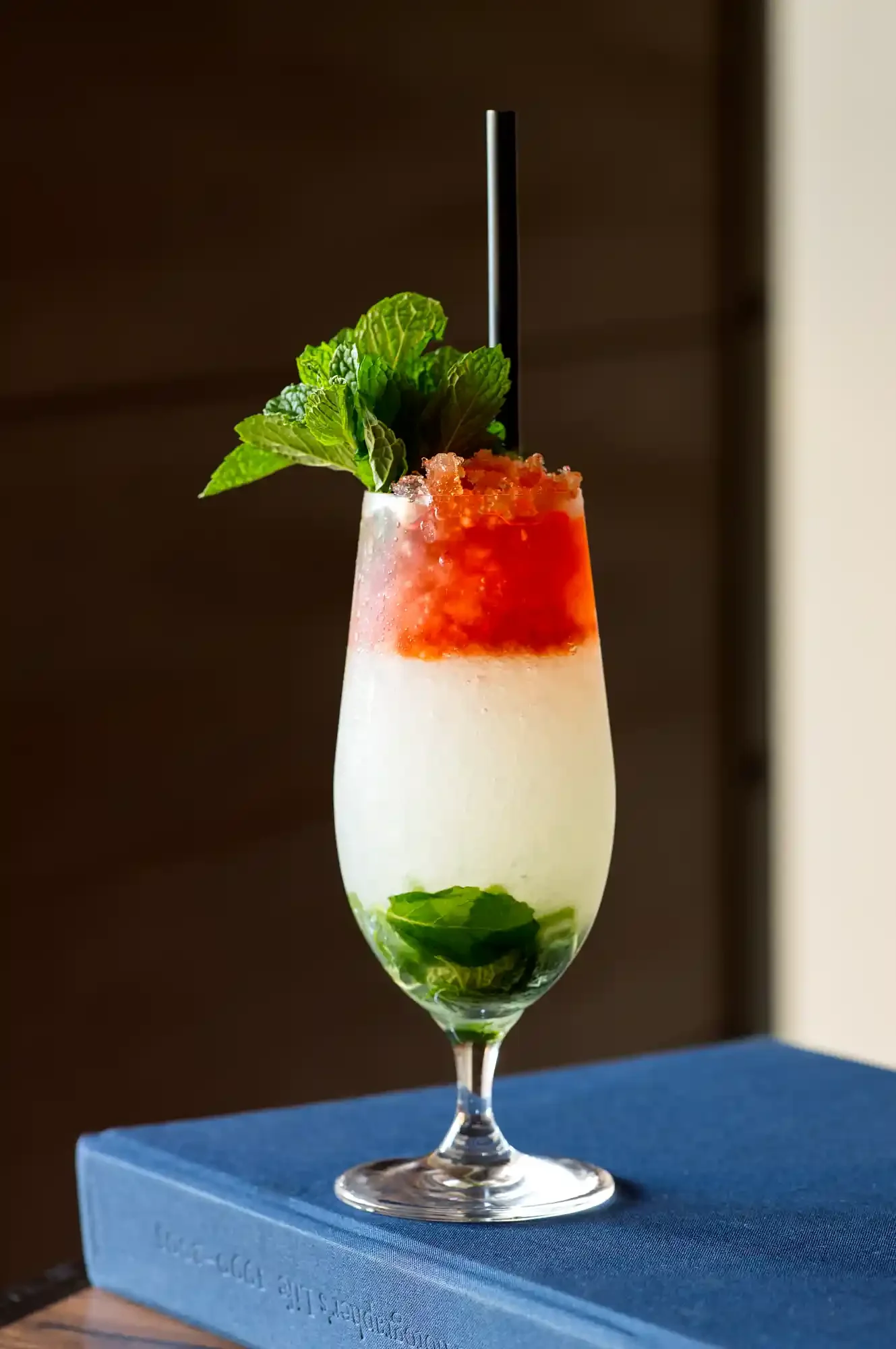 A layered Queen's Park cocktail in a tall glass with mint leaves, crushed ice, and a straw, featuring a white base, a red middle layer, and garnished with fresh mint and a straw. By Philadelphia, PA drink photographer.