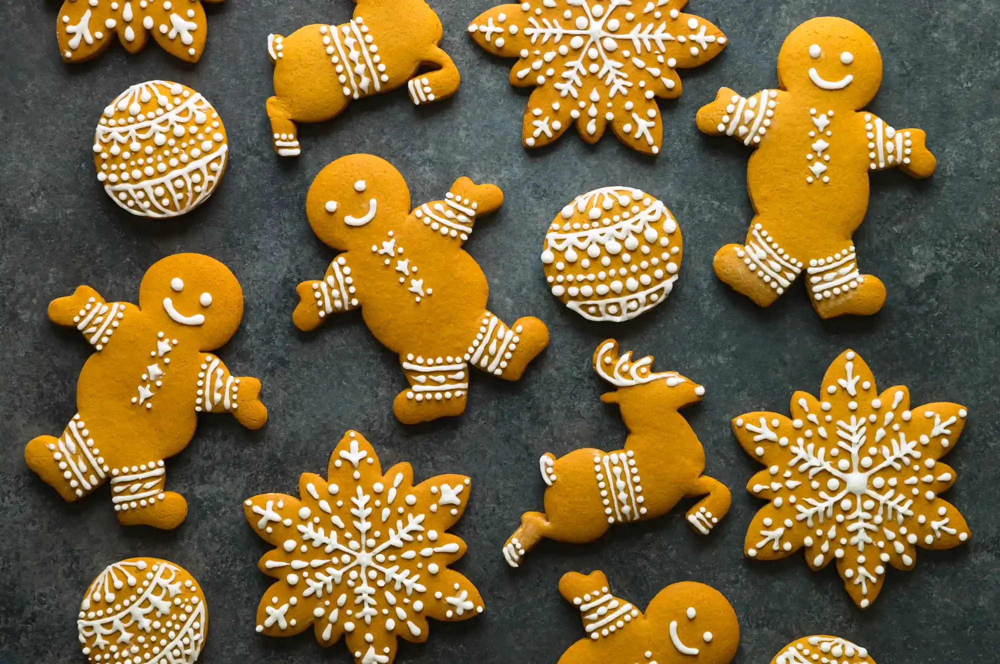 Assorted Christmas cookies on a dark surface, including gingerbread men decorated with white icing, decorated snowflakes, and intricate icing patterns. By New Jersey & Philadelphia, PA food photographer & food stylist team Bartholomew Studio.