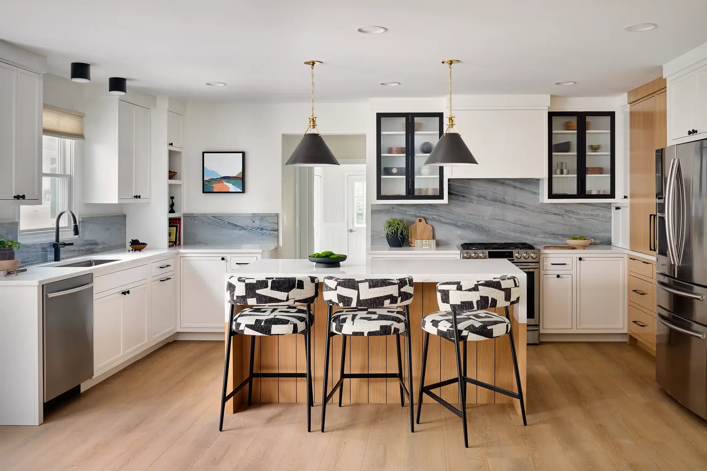 Modern kitchen with white cabinets, marble backsplash, stainless steel appliances, black and gold pendant lights designed by Restart Homes.