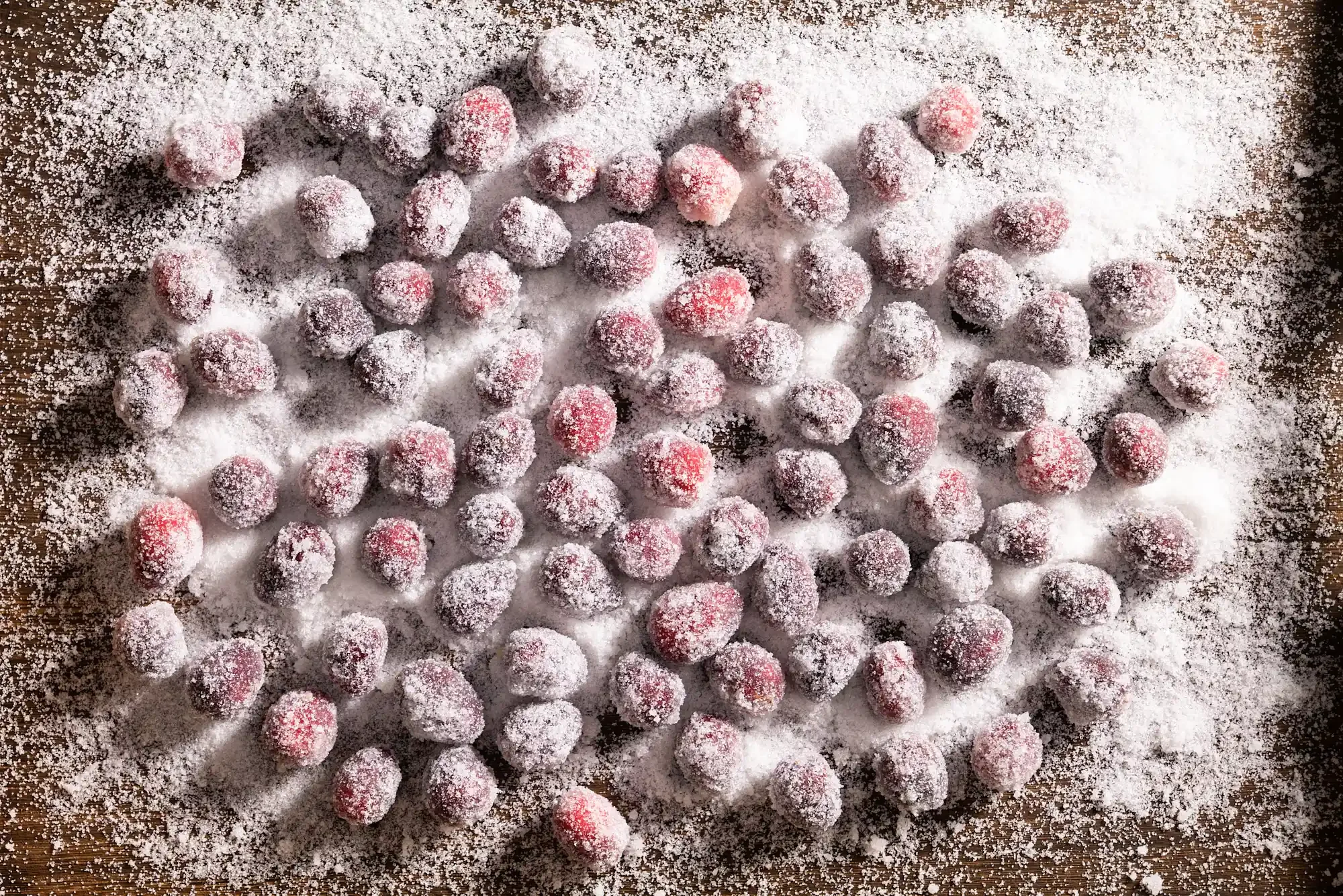 Frozen red berries dusted with powdered sugar, scattered on a wooden surface. By NJ & NYC food photographer & food stylist team Bartholomew Studio.