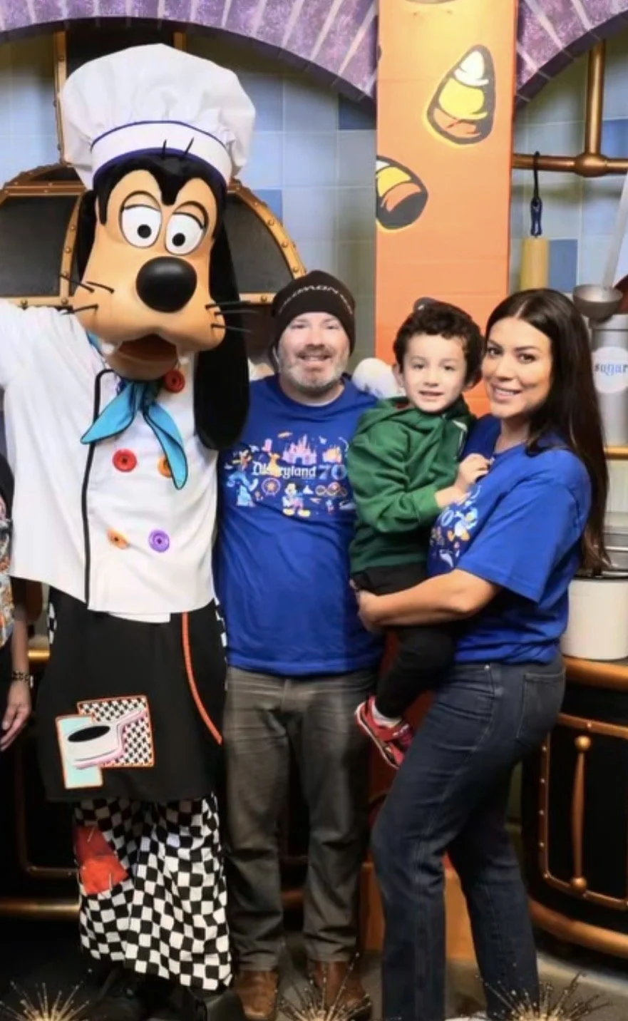 Family posing with Pluto dressed as a chef at Disneyland, with colorful background and kitchen-themed decorations.