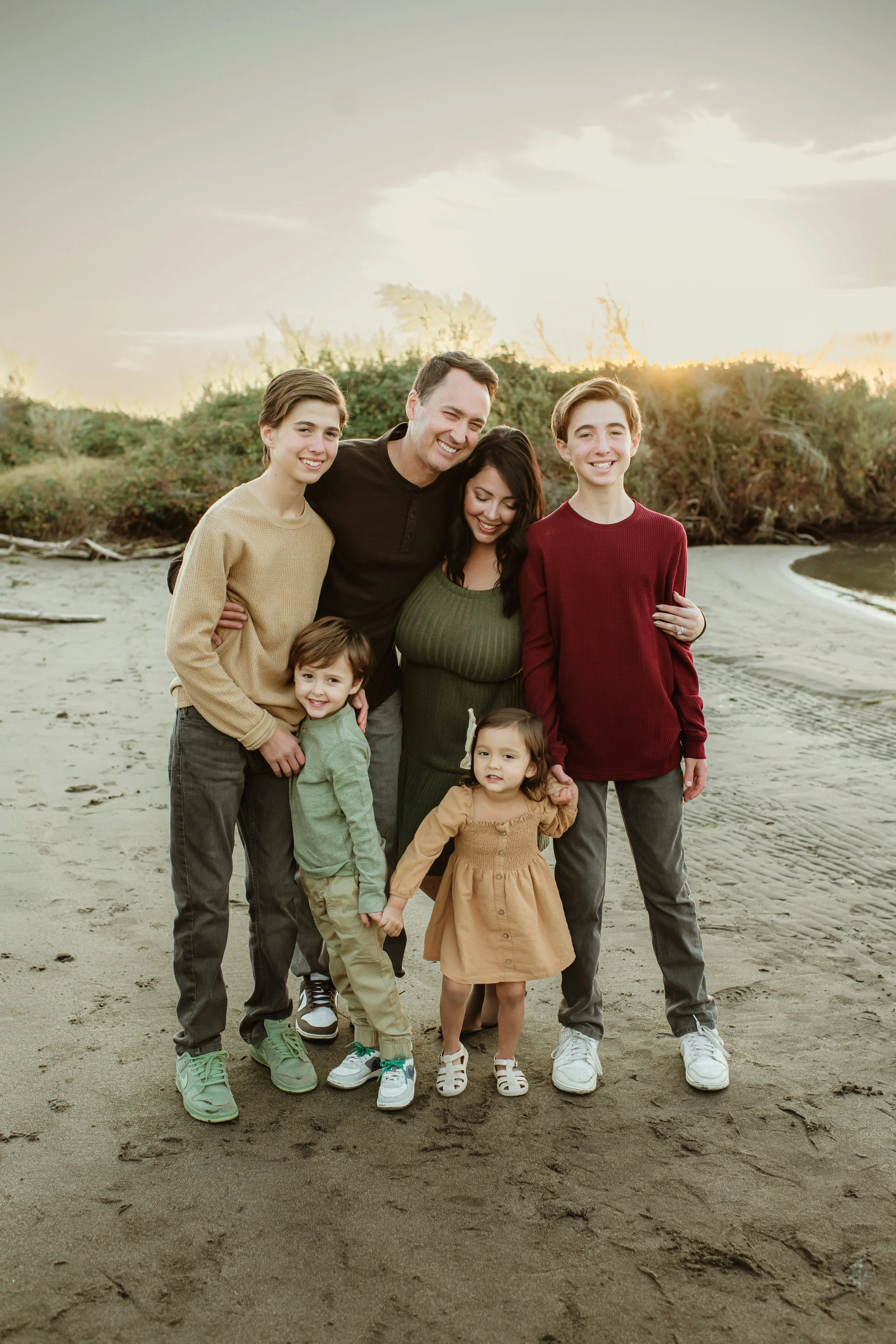 Family of seven standing on sandy beach during sunset, smiling.