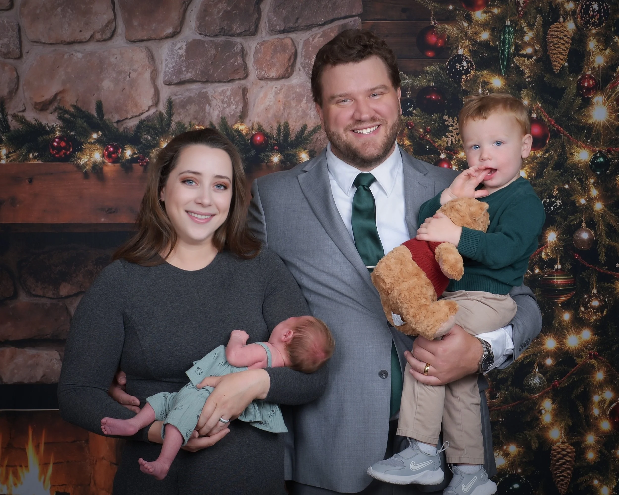 A family with a woman, man, and two young children standing in front of a decorated Christmas tree and fireplace