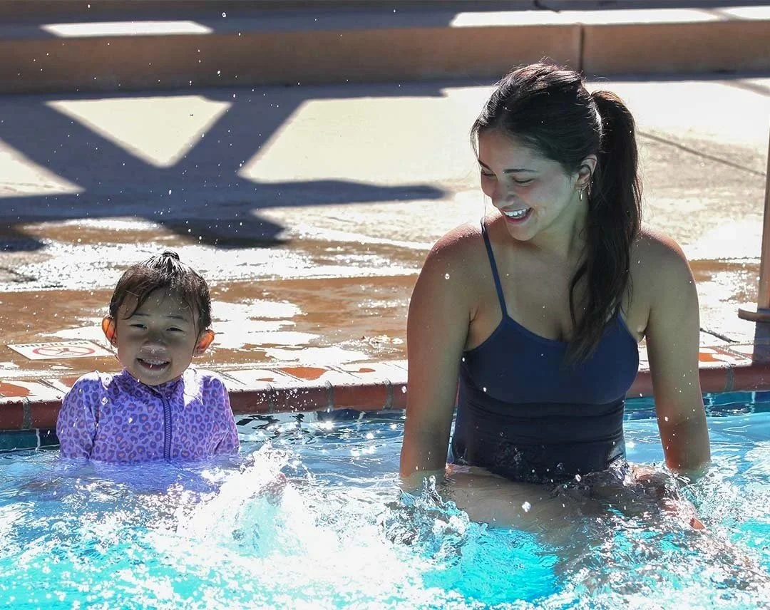 A smiling young woman and a small girl enjoying their time in a swimming pool together.