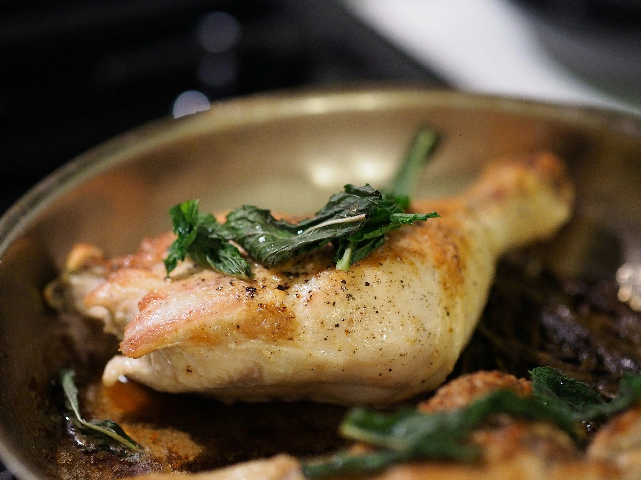 Close-up of a cooked chicken breast topped with wilted greens in a cast iron skillet.