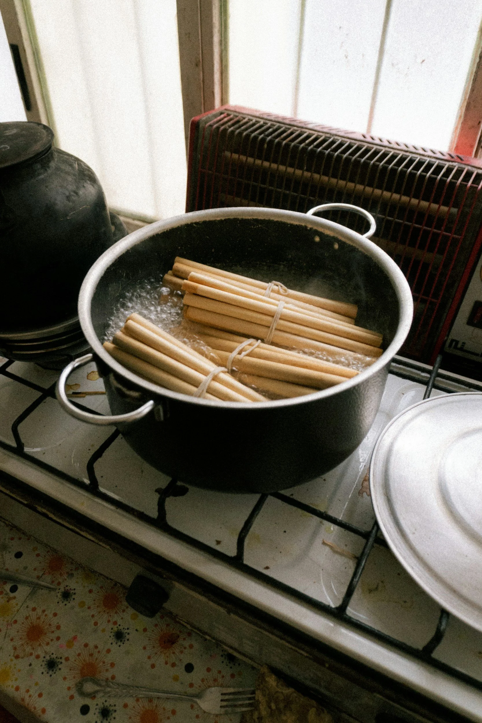 Pot on stove with bundles of uncooked spaghetti in boiling water, kitchen scene with stove, counter, and utensils.