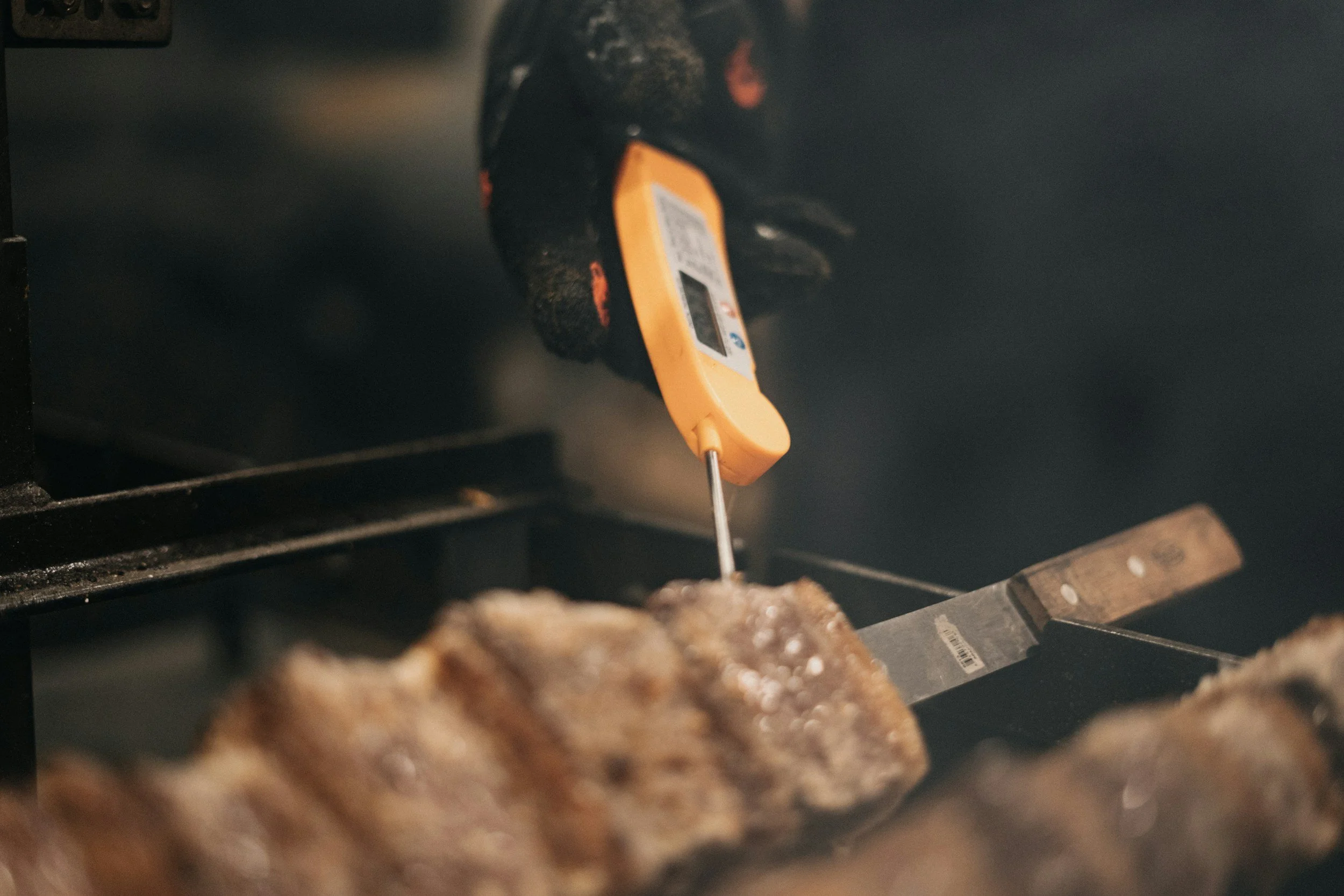 Close-up of a grill with meat patties cooking, and a yellow meat thermometer inserted into one of the patties.