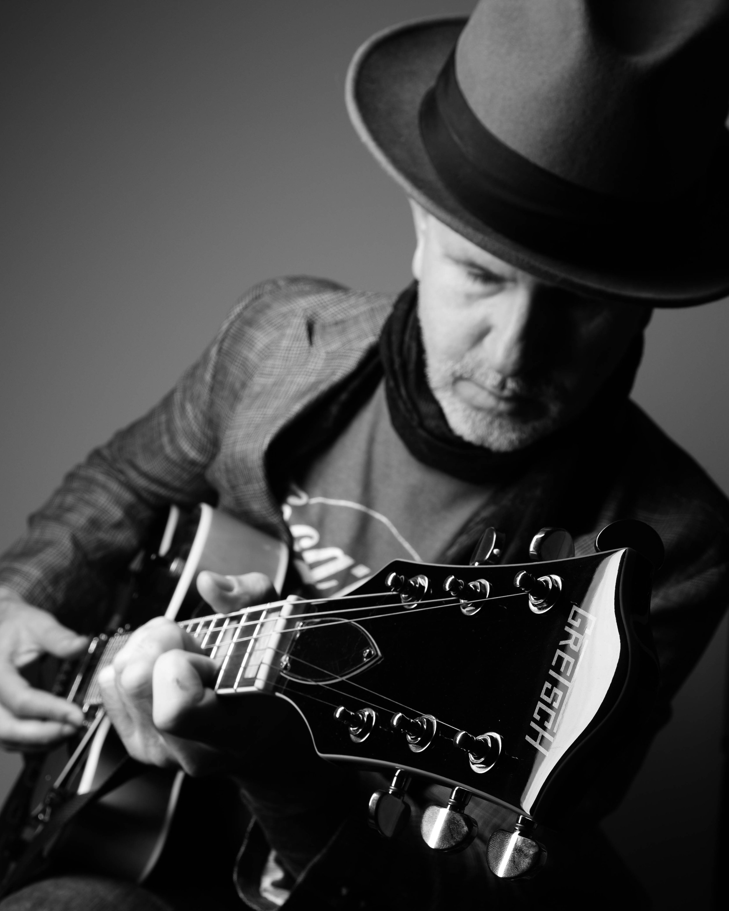 Singer & guitarist of The Thrift Store Dadnys,  wearing a hat and scarf playing an electric guitar in black and white.