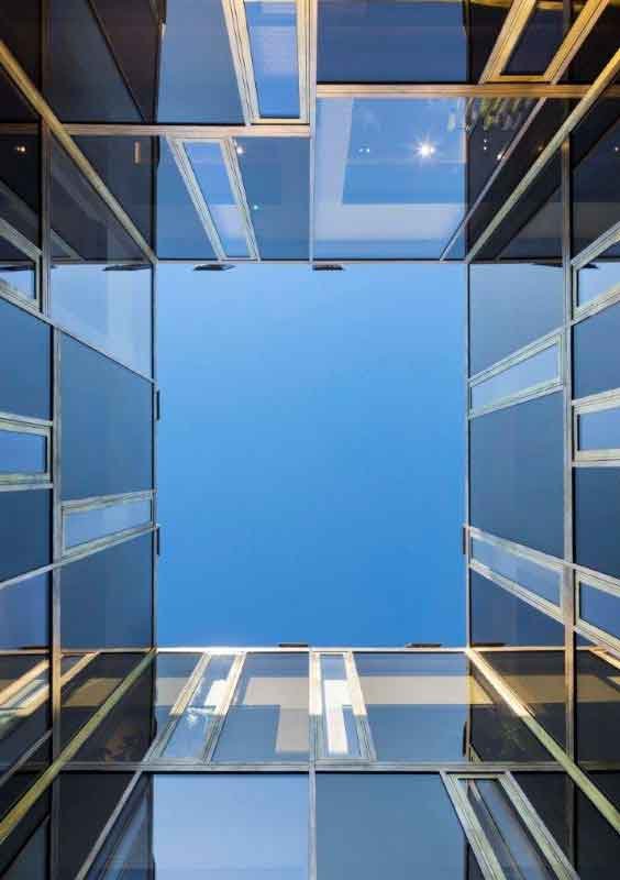 View looking up at the sky through an open square courtyard surrounded by modern glass and metal apartment buildings.