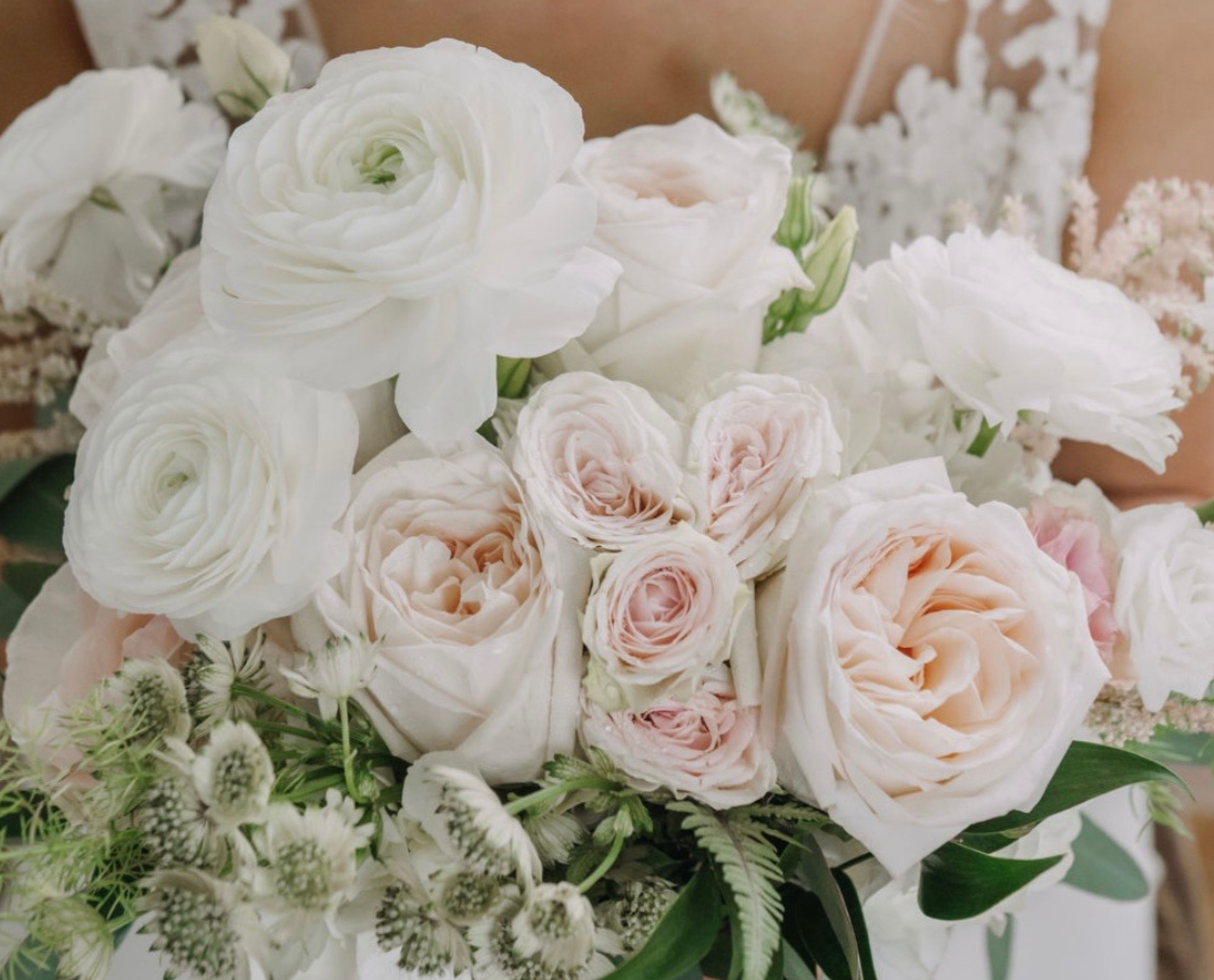A bouquet of white and pale pink roses with greenery.