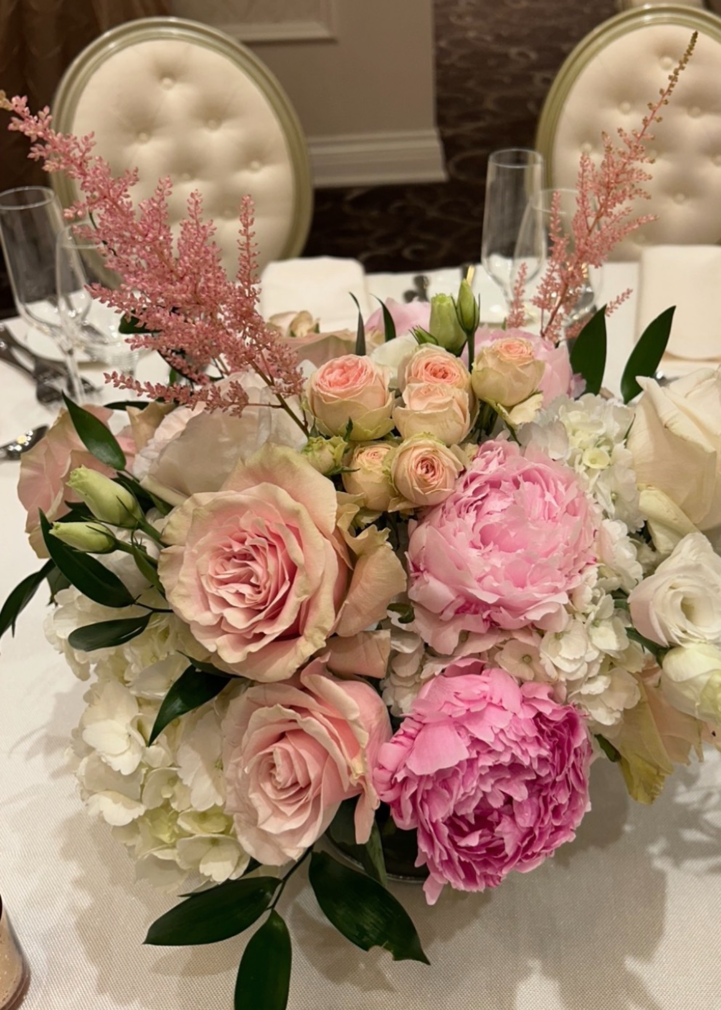 Elegant floral centerpiece with pink roses, peonies, and white hydrangeas on a banquet table, set for a formal event.