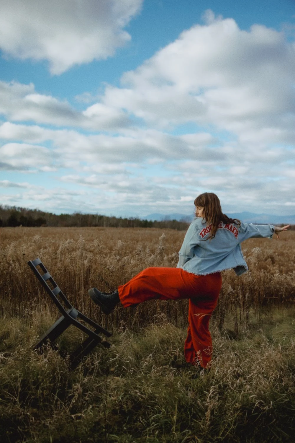Editorial branding portrait of female artist kicking over black chair in huge field