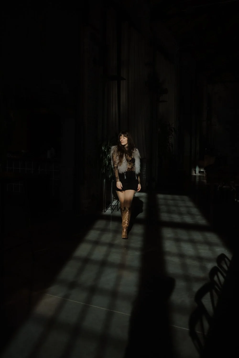 Editorial branding portrait of female entrepreneur dressed to impress walking in harsh shadows of industrial windows