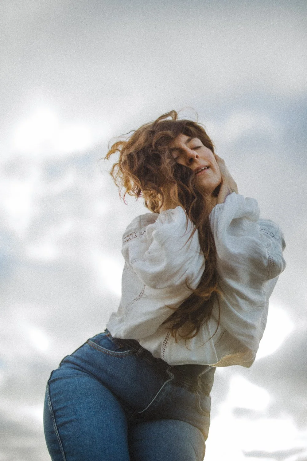 Editorial branding portrait of female entrepreneur framed against the big sky holding her head in hands