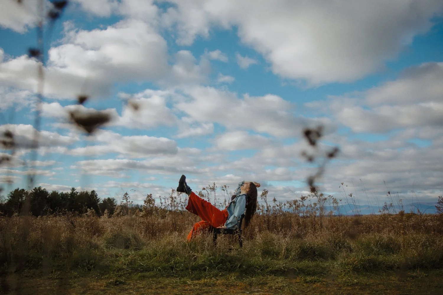 Editorial branding portrait of female entrepreneur sitting in a chair in a field with bright blue skies