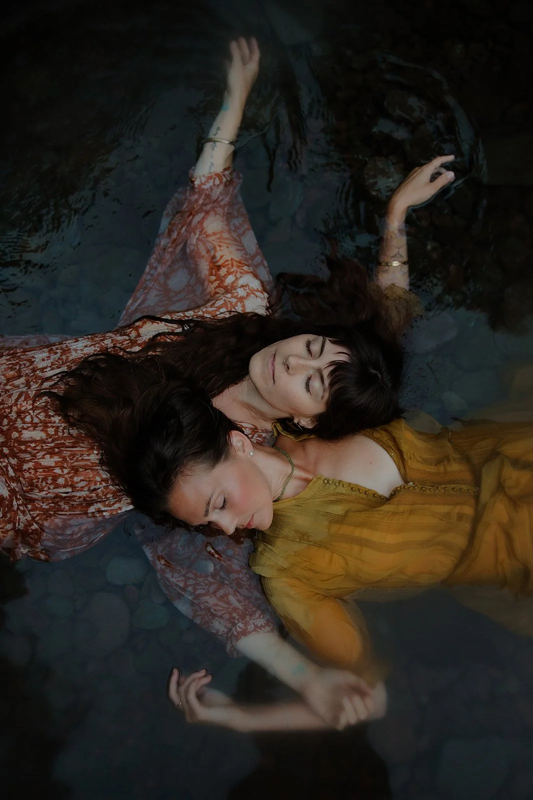 Editorial branding portrait of female entrepreneurs calmly laying in the river with heads on each others shoulder
