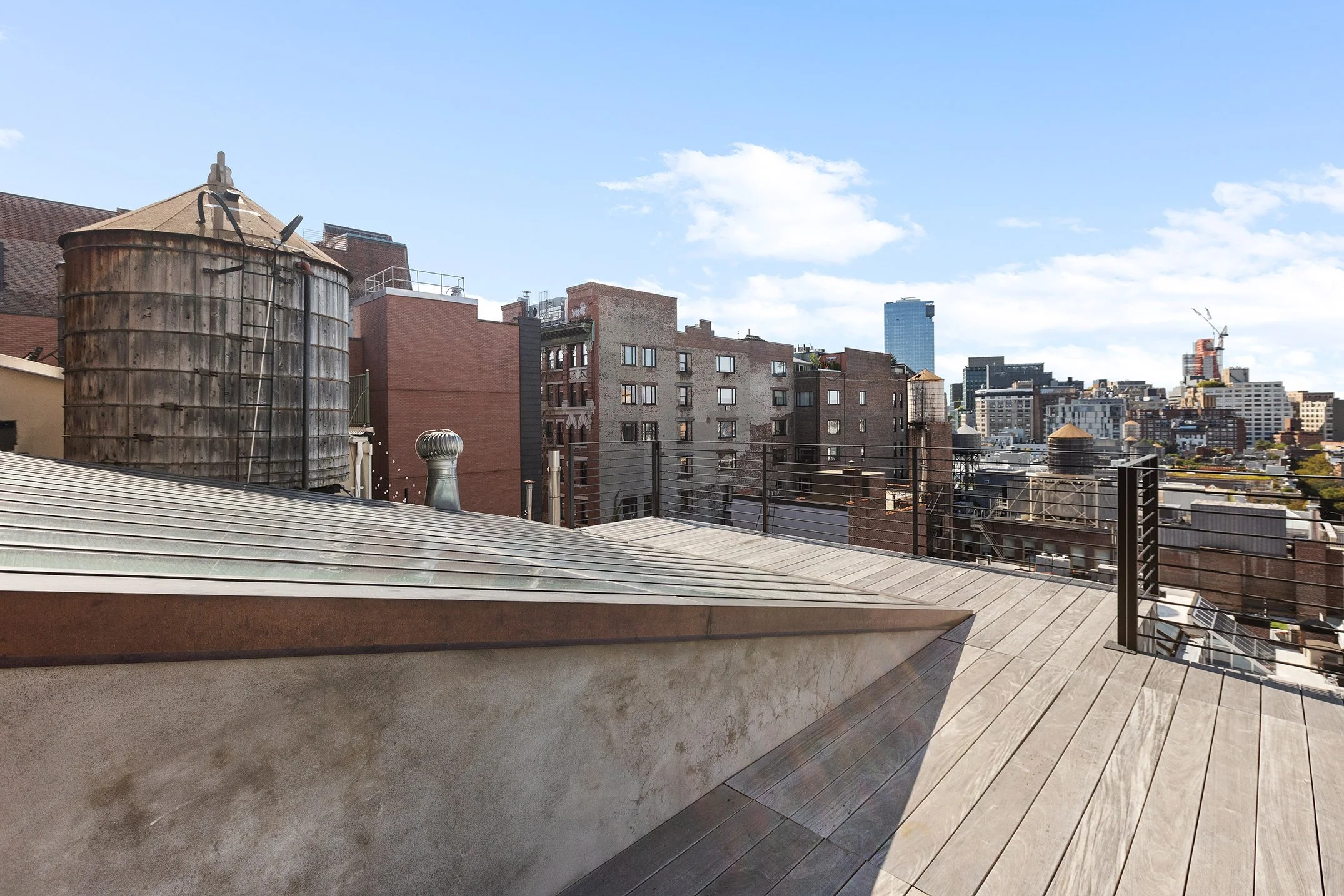 Rooftop view overlooking city buildings under clear blue sky with some clouds