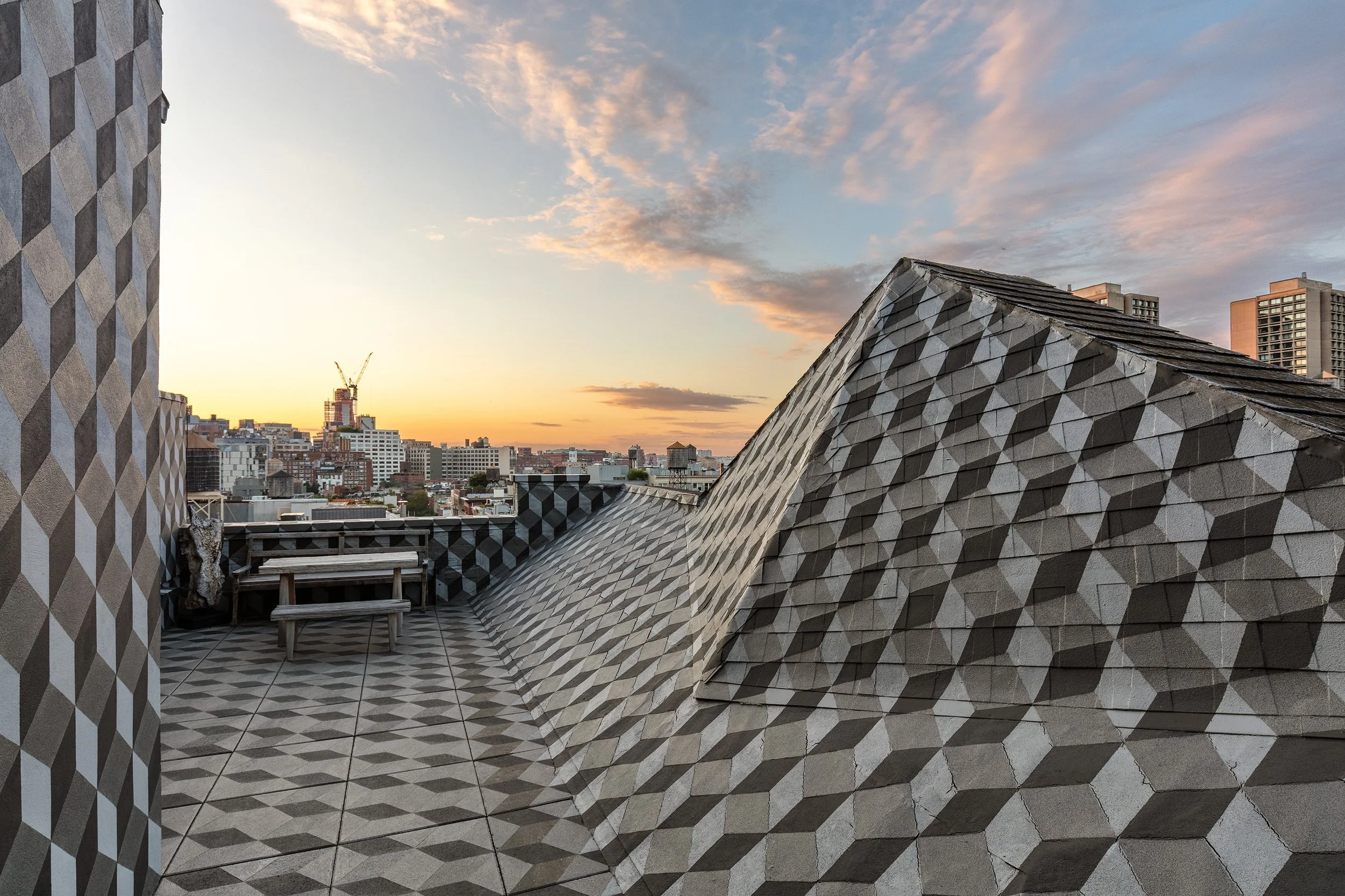City skyline at sunset with geometric patterned rooftop and buildings in the background.