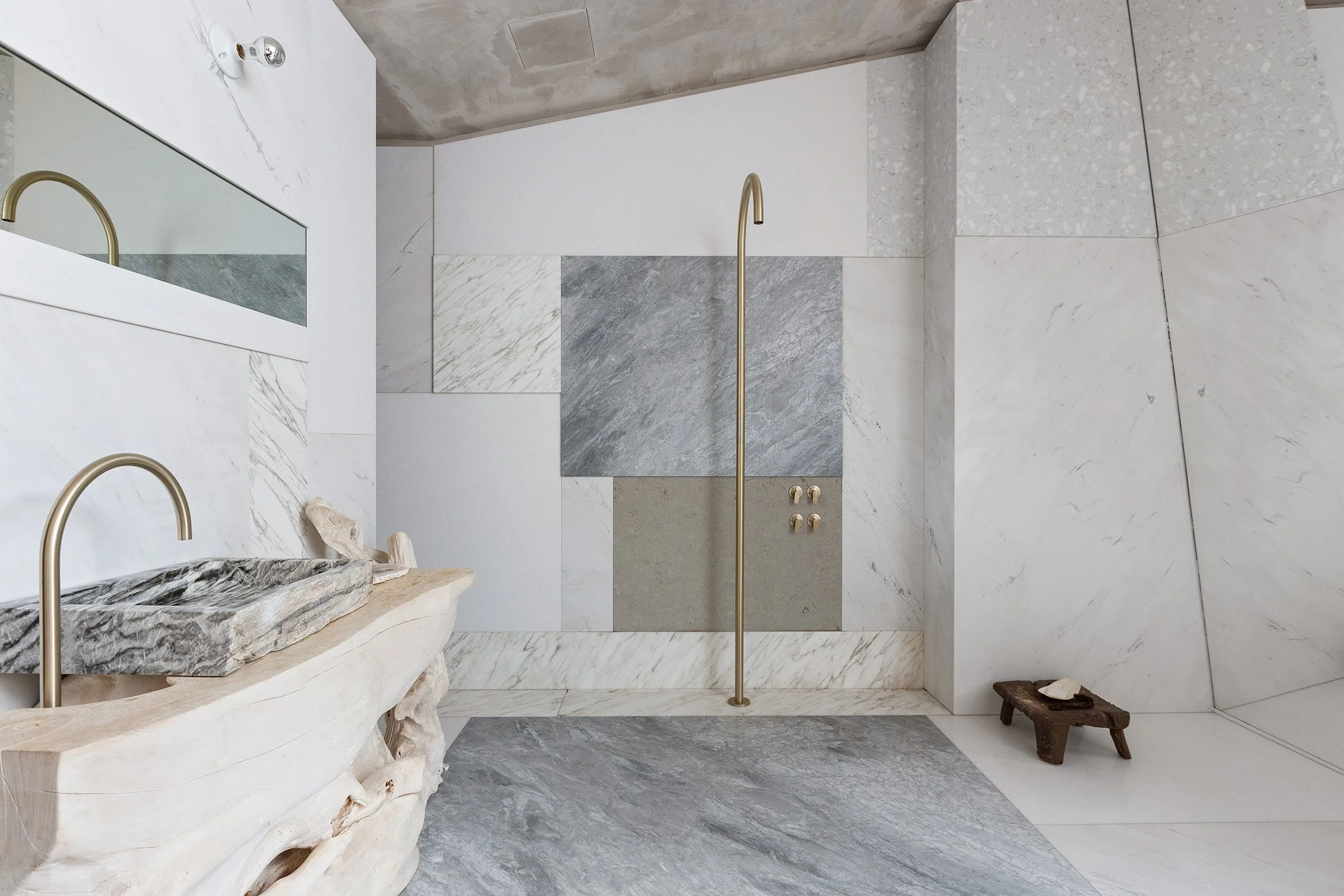 Modern bathroom with marble walls, a stone bathtub, a large mirror, and brass fixtures.