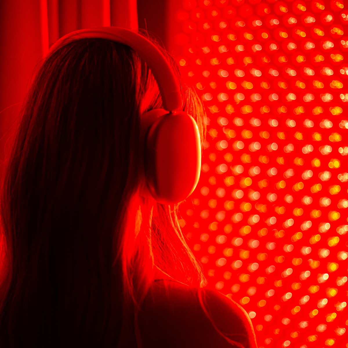 A person with long hair wearing headphones in front of a red, illuminated, bokeh background.