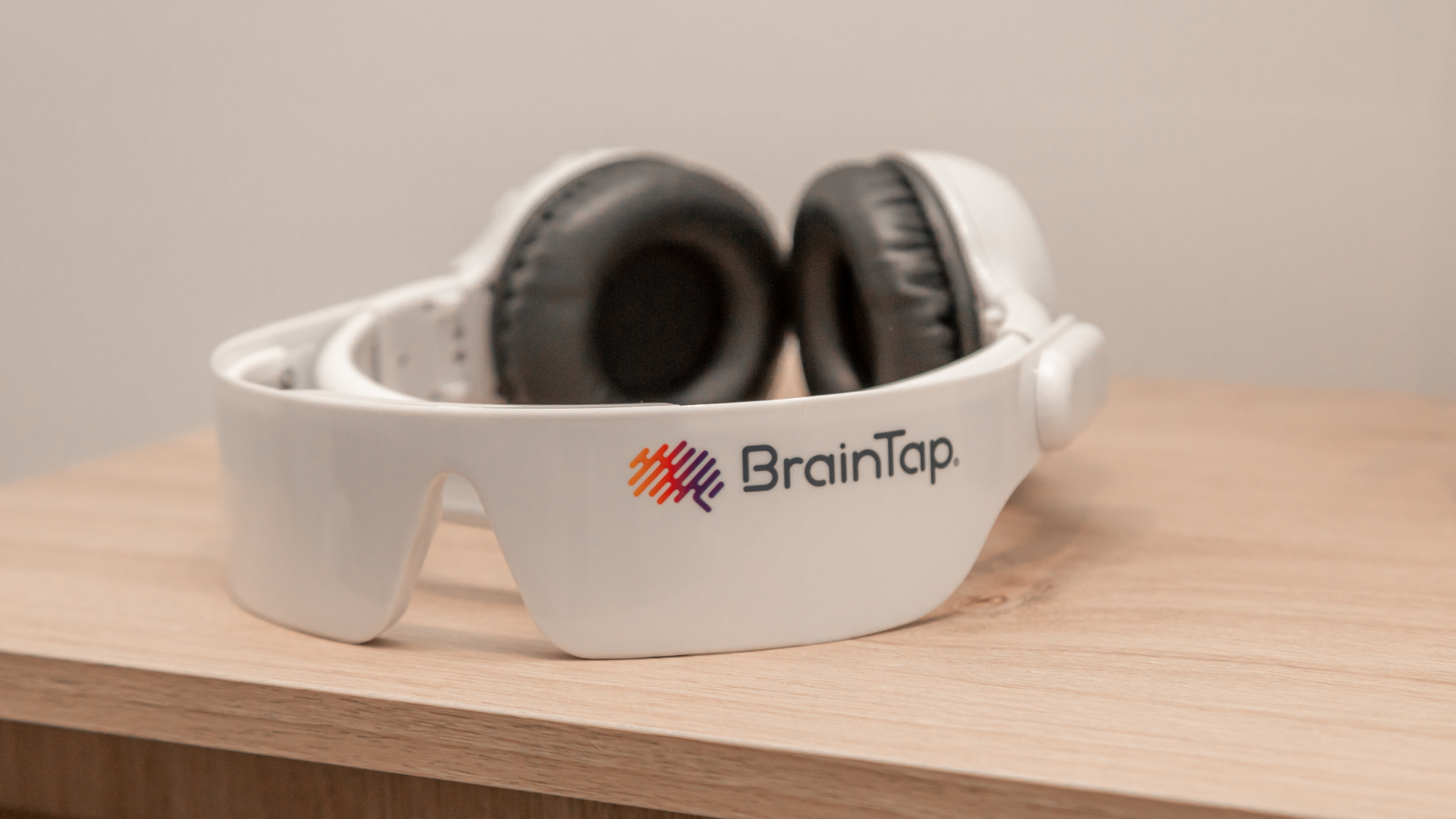 White BrainTap headset with black ear cushions resting on a wooden surface