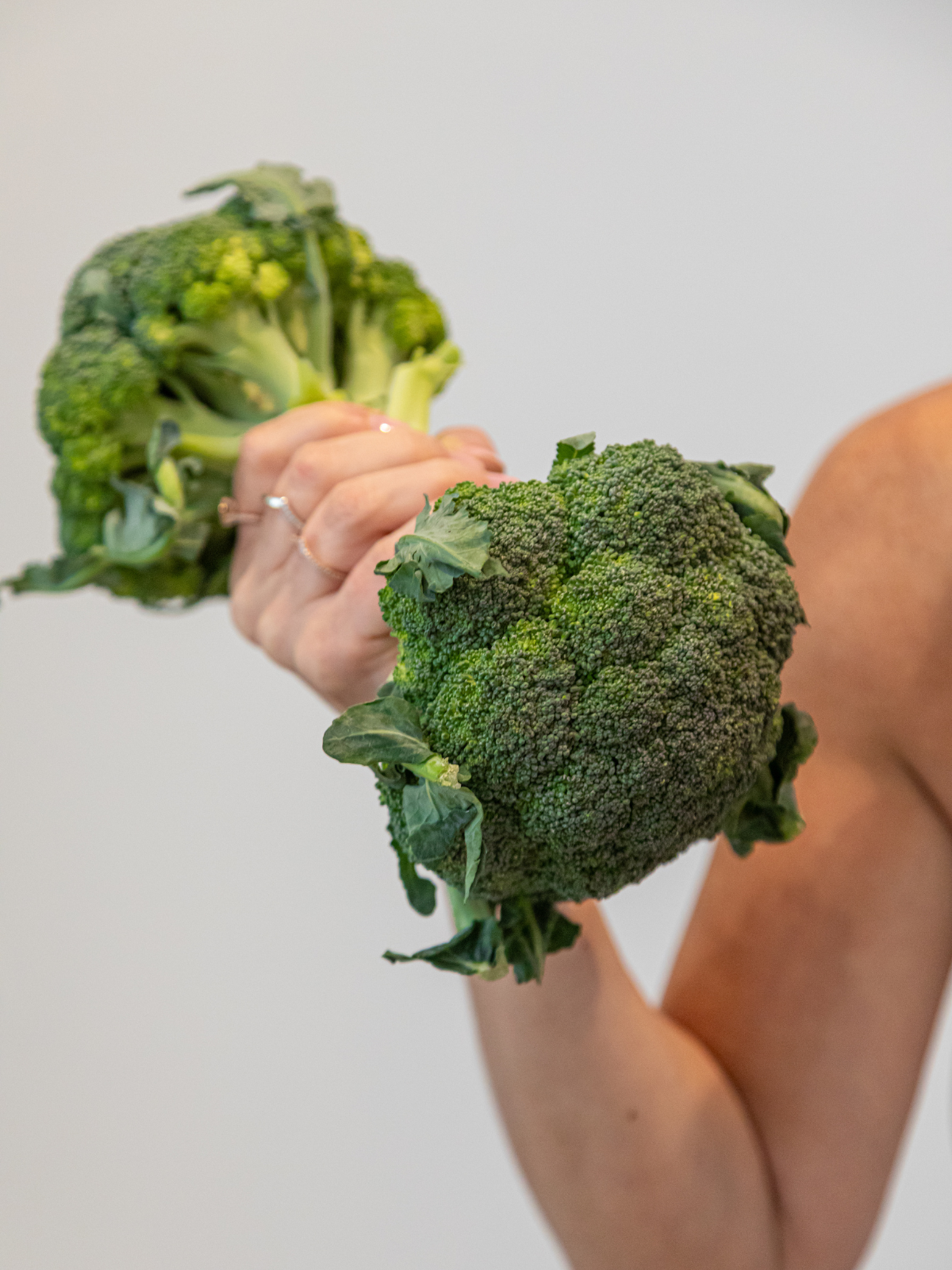 Person holding two large broccoli florets against a plain background.