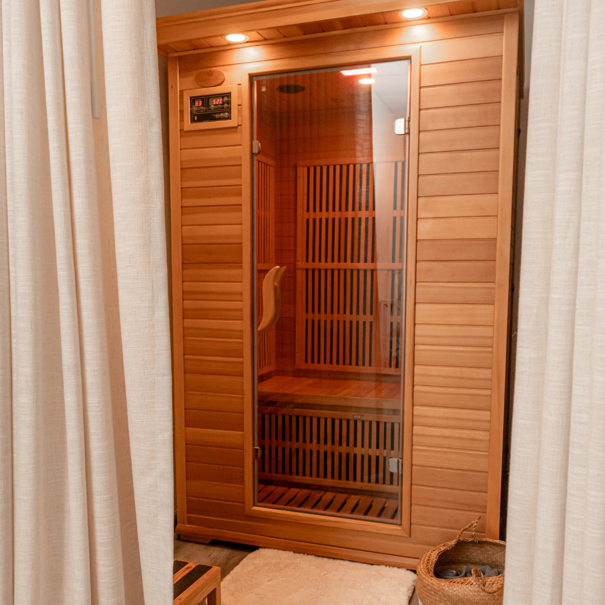 A wooden sauna with a glass door, inside benches, and a digital temperature display on the wall.