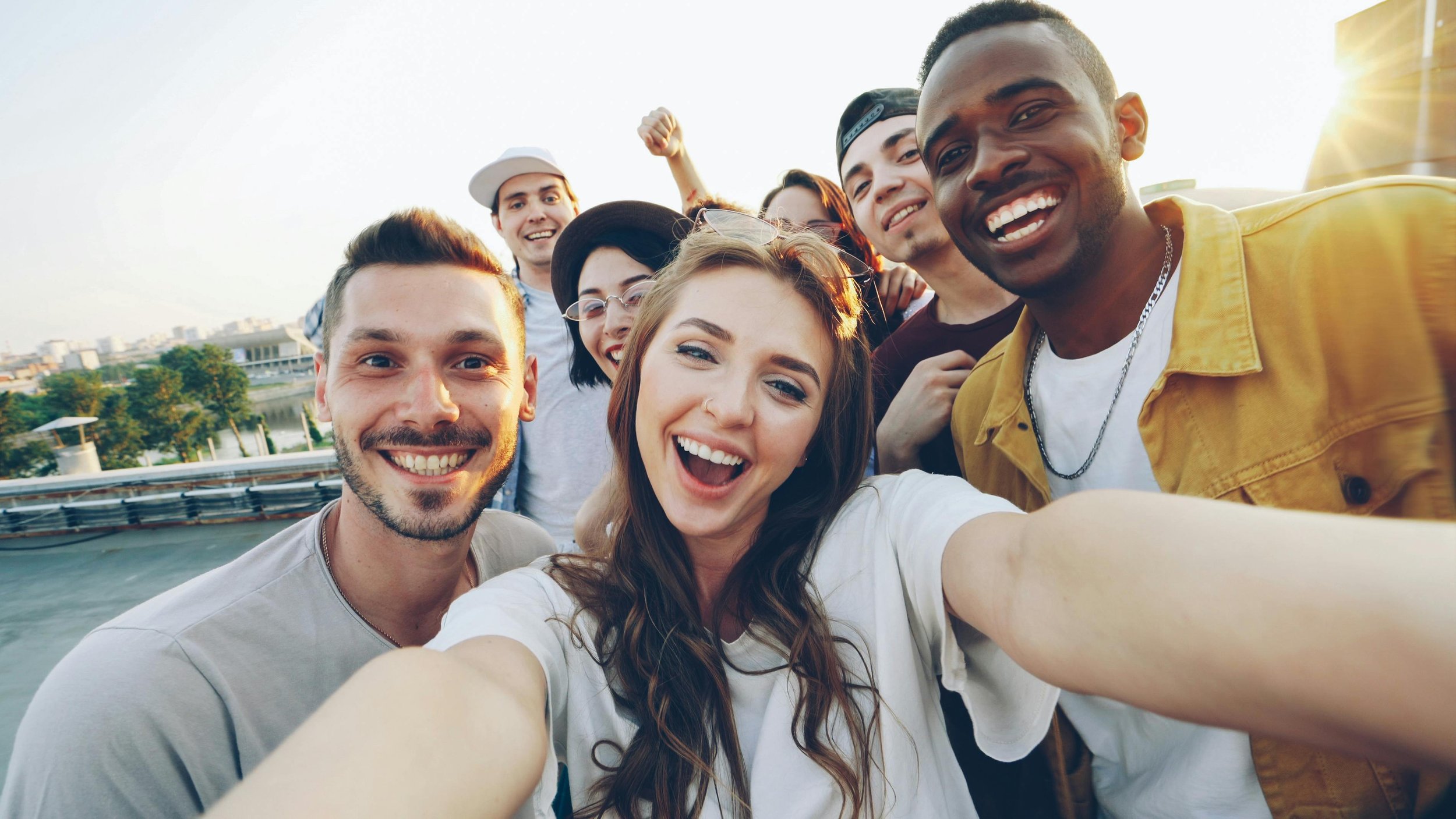 A group of diverse friends taking a selfie outdoors during sunset, smiling and enjoying each other's company.