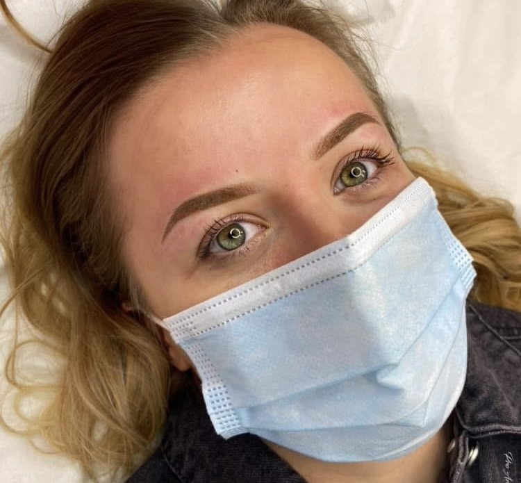 Close-up of a woman with blonde hair wearing a blue face mask and looking up at the camera.