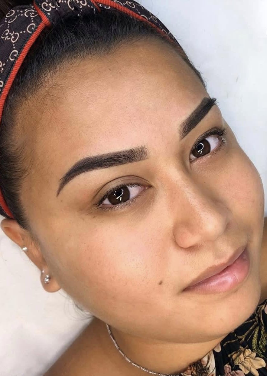 Close-up of a woman with well-groomed eyebrows, earrings, and a headband, smiling slightly and looking at the camera.
