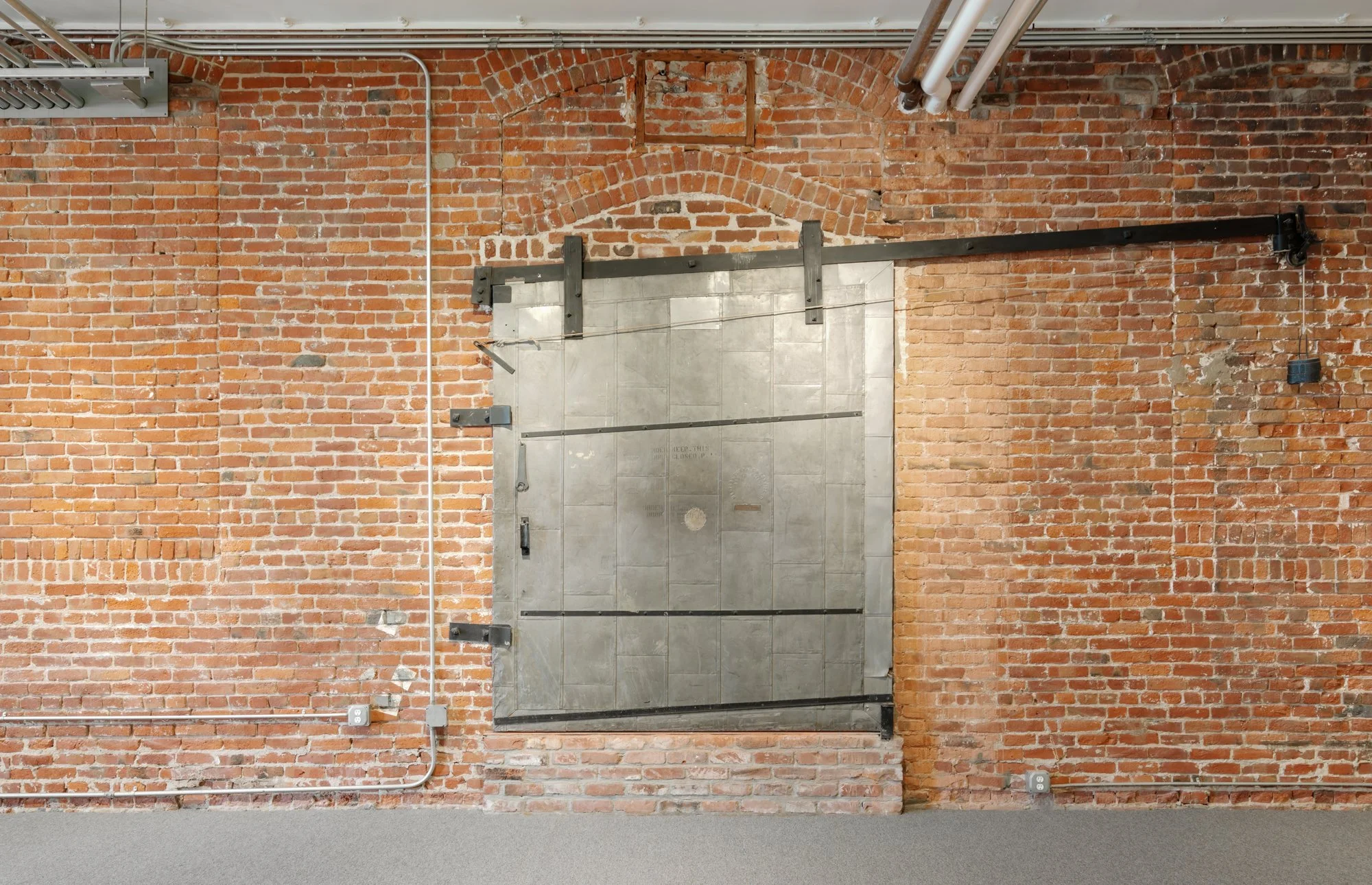 A metal sliding door installed on a brick wall with exposed pipes and electrical wiring.