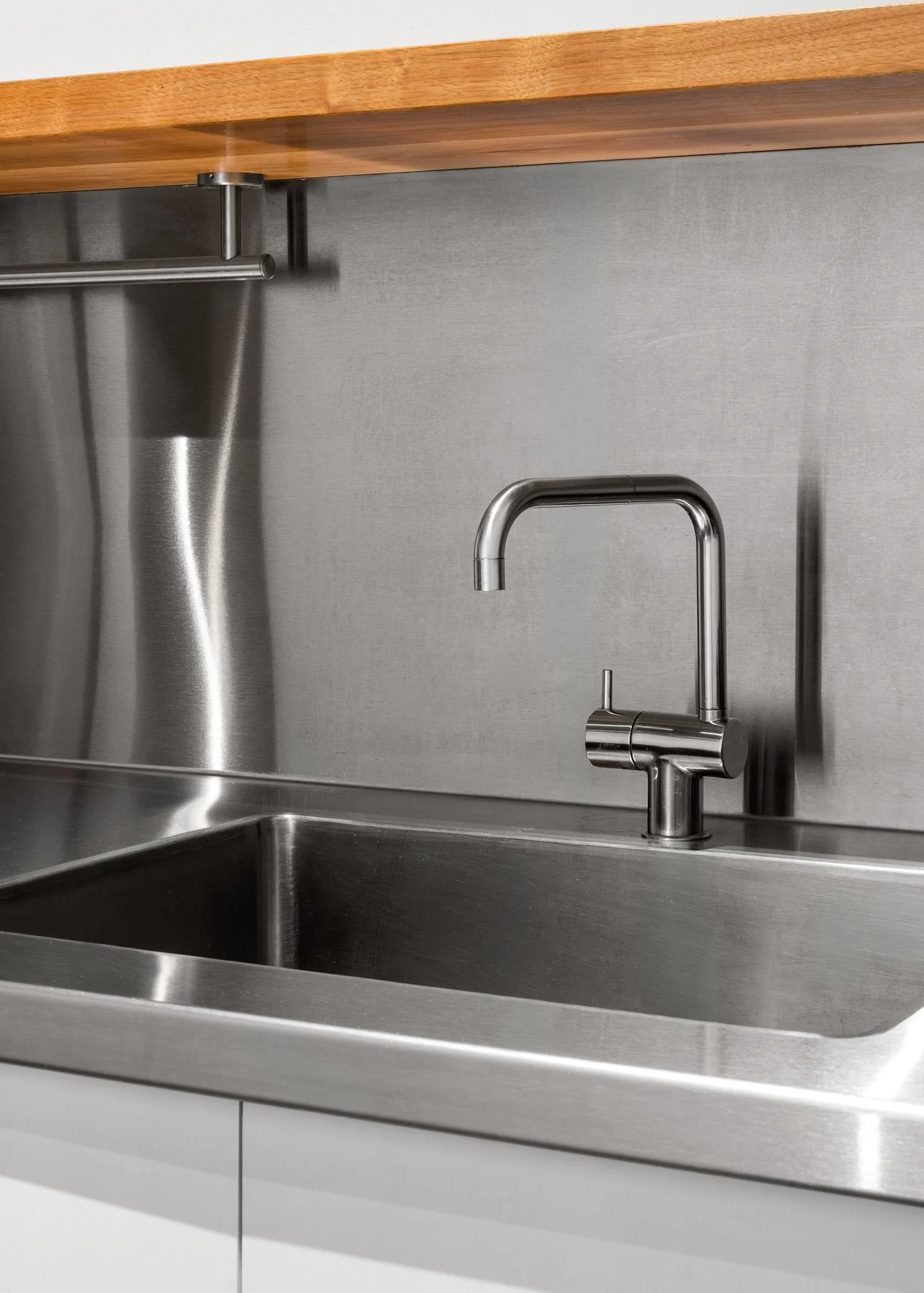 A stainless steel kitchen sink with a modern pull-out faucet, mounted under a wooden countertop with a grey backsplash.
