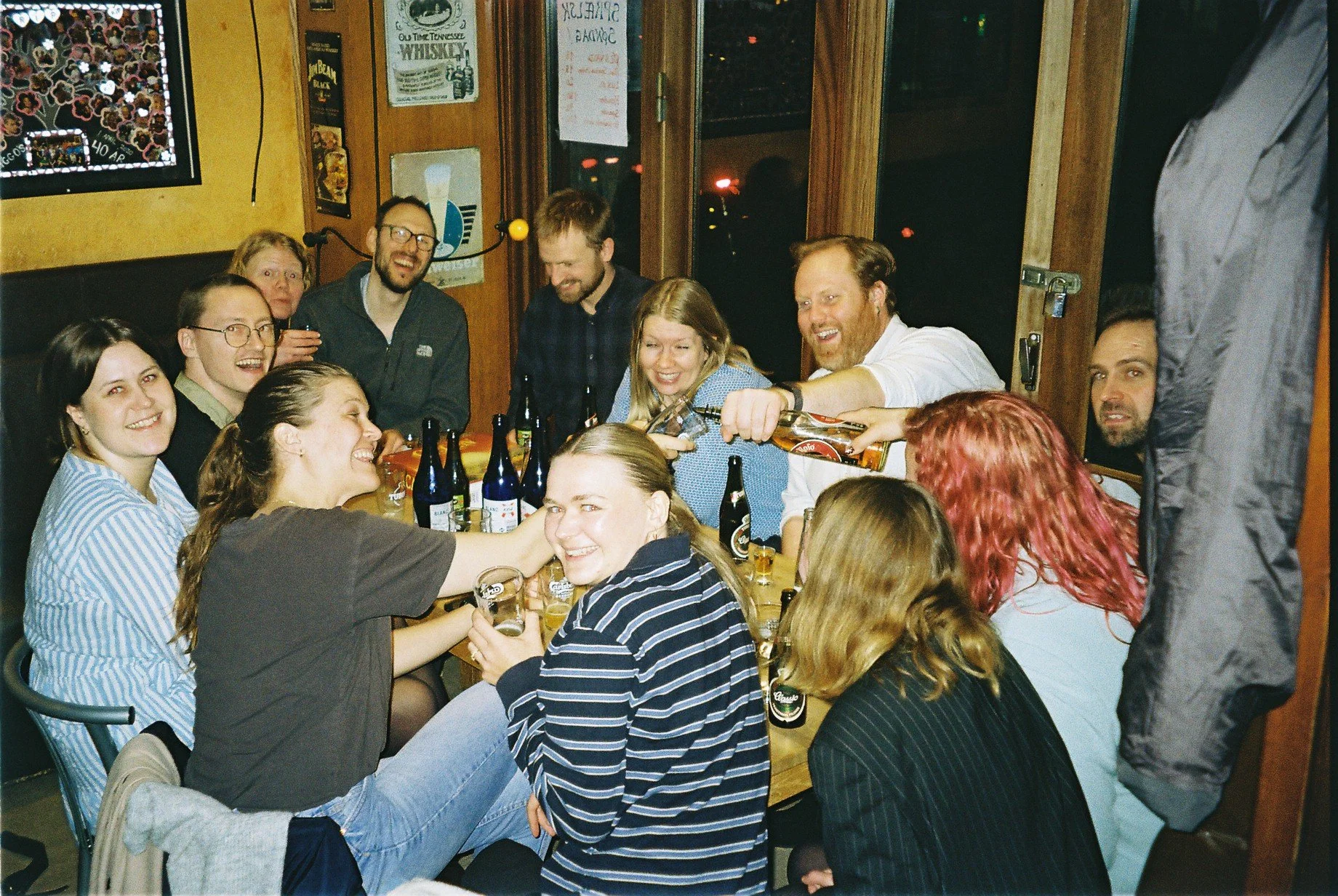 Gruppe venner har en fest i en bar, hvor nogle drikker øl, og der er masser af smil og latter.