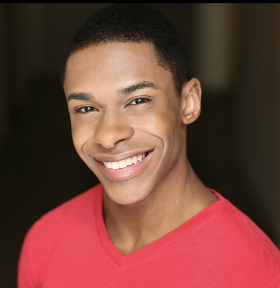A smiling man in a burgundy sweater poses against a dark background.
