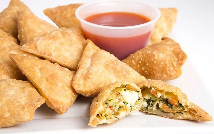 Plate of golden fried samosas with a side of red tamarind dipping sauce.
