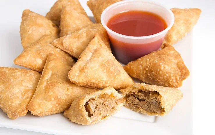 Fried beef samosas with a side of tamarind chutney sauce on a white plate.