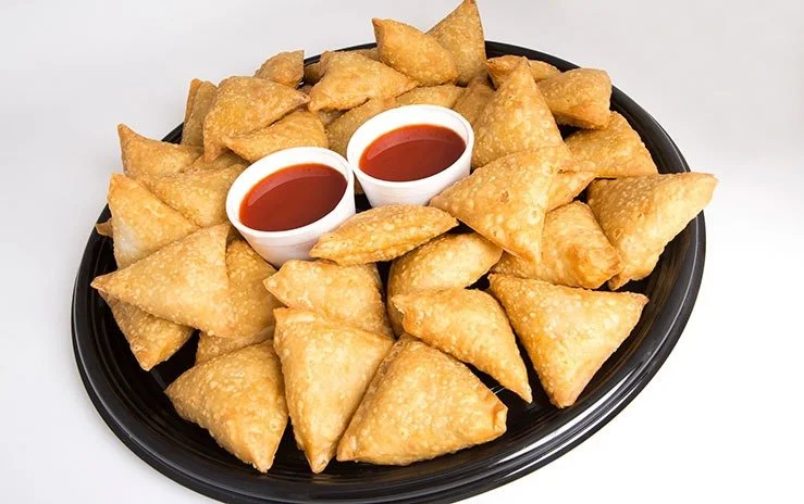 A black tray filled with fried samosas and two small cups of tamarind dipping sauce.
