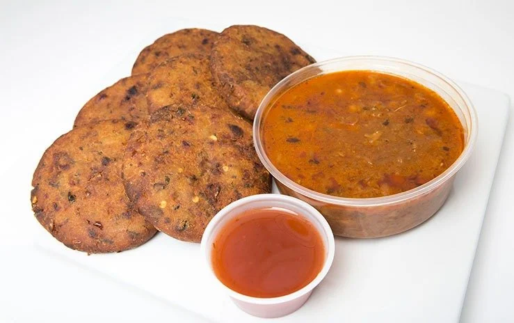 Plate with three fried aloo tikki crispy potato cakes, a bowl of chickpea curry, and a small bowl of red tamarind chutney.