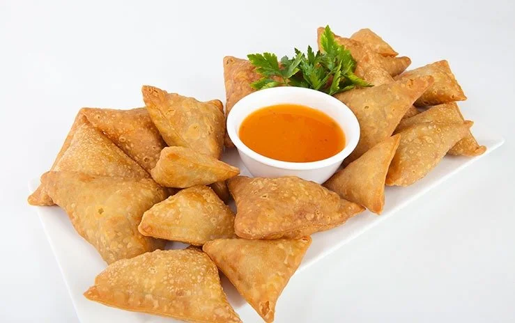 Plate of golden fried samosas with a side of red tamarind dipping sauce.