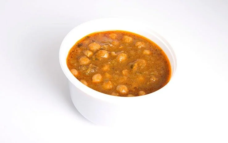 White bowl filled with chickpea curry on a white surface.