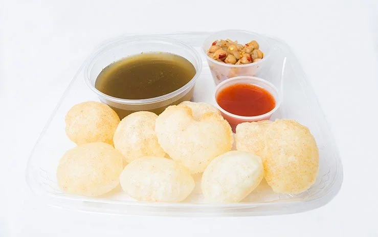 A plate of pani puri with spicy water, tamarind chutney, and spicy chickpea filling.
