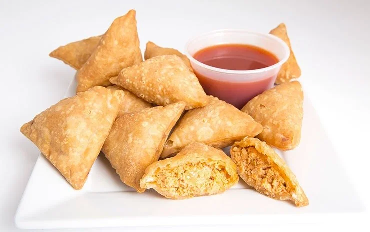 Plate of golden-fried samosas with a side of red dipping sauce.