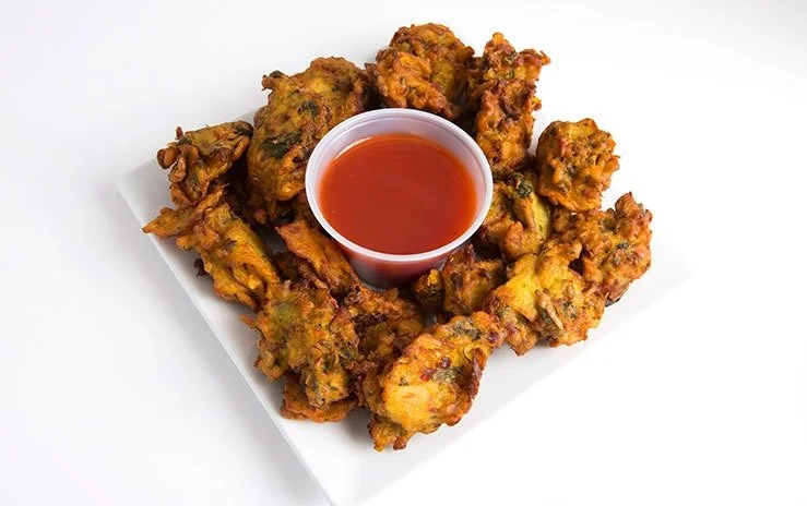 Fried vegetable pakoras with a side of red dipping sauce on a white plate