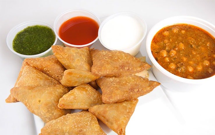 Plate of samosas with various dipping sauces and a bowl of chickpea curry.
