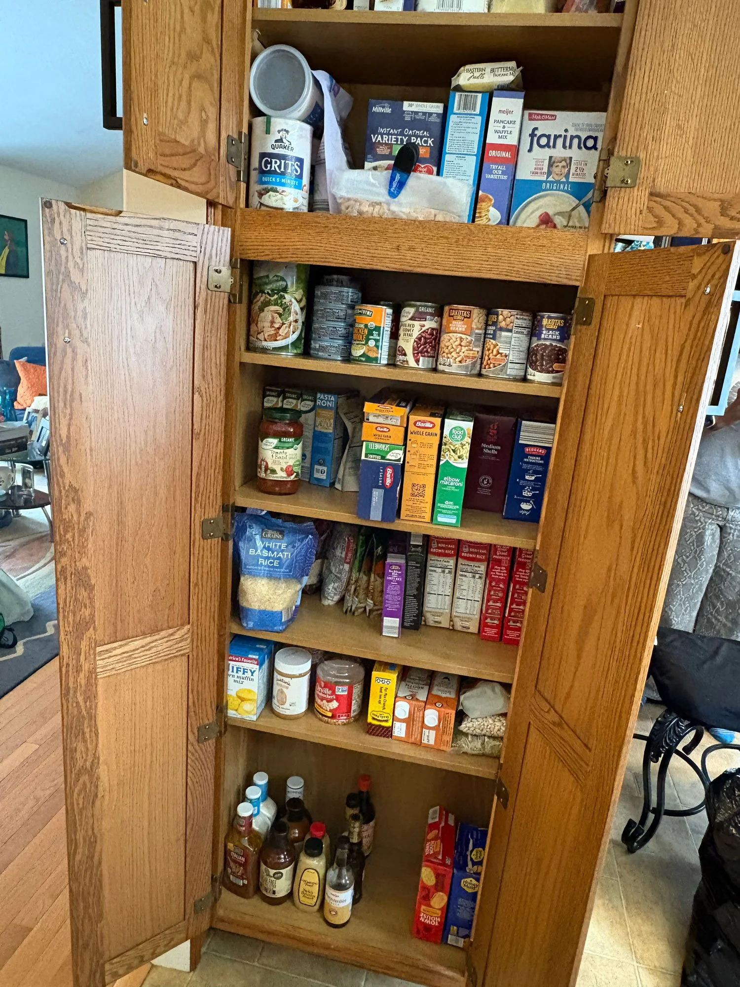 Open wooden kitchen cabinet with shelves containing canned goods, dry foods, sauces, and condiments.
