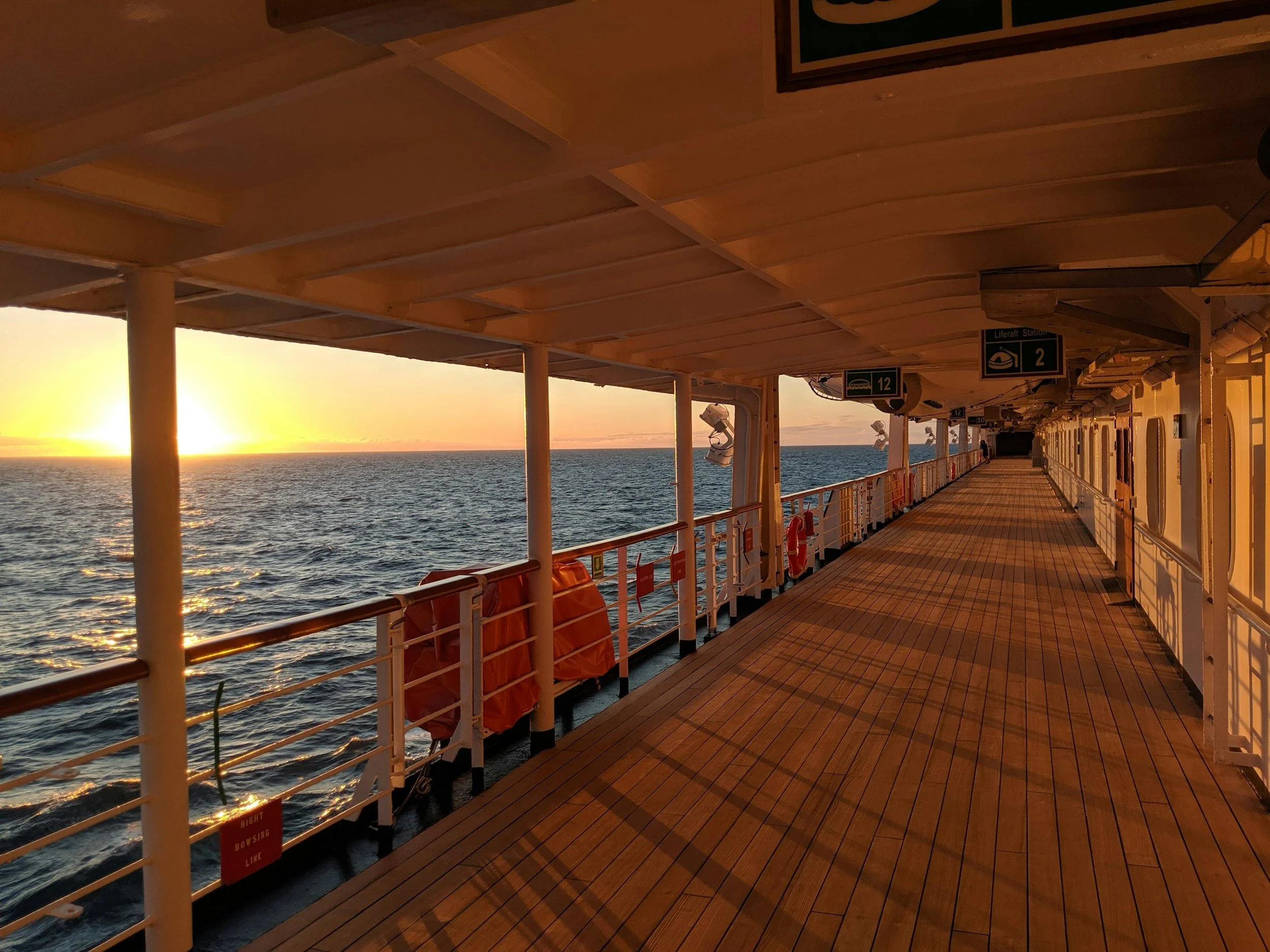 View of the ocean at sunset from the deck of a cruise ship, with the sunlight reflecting on the sea and the empty ship corridor.