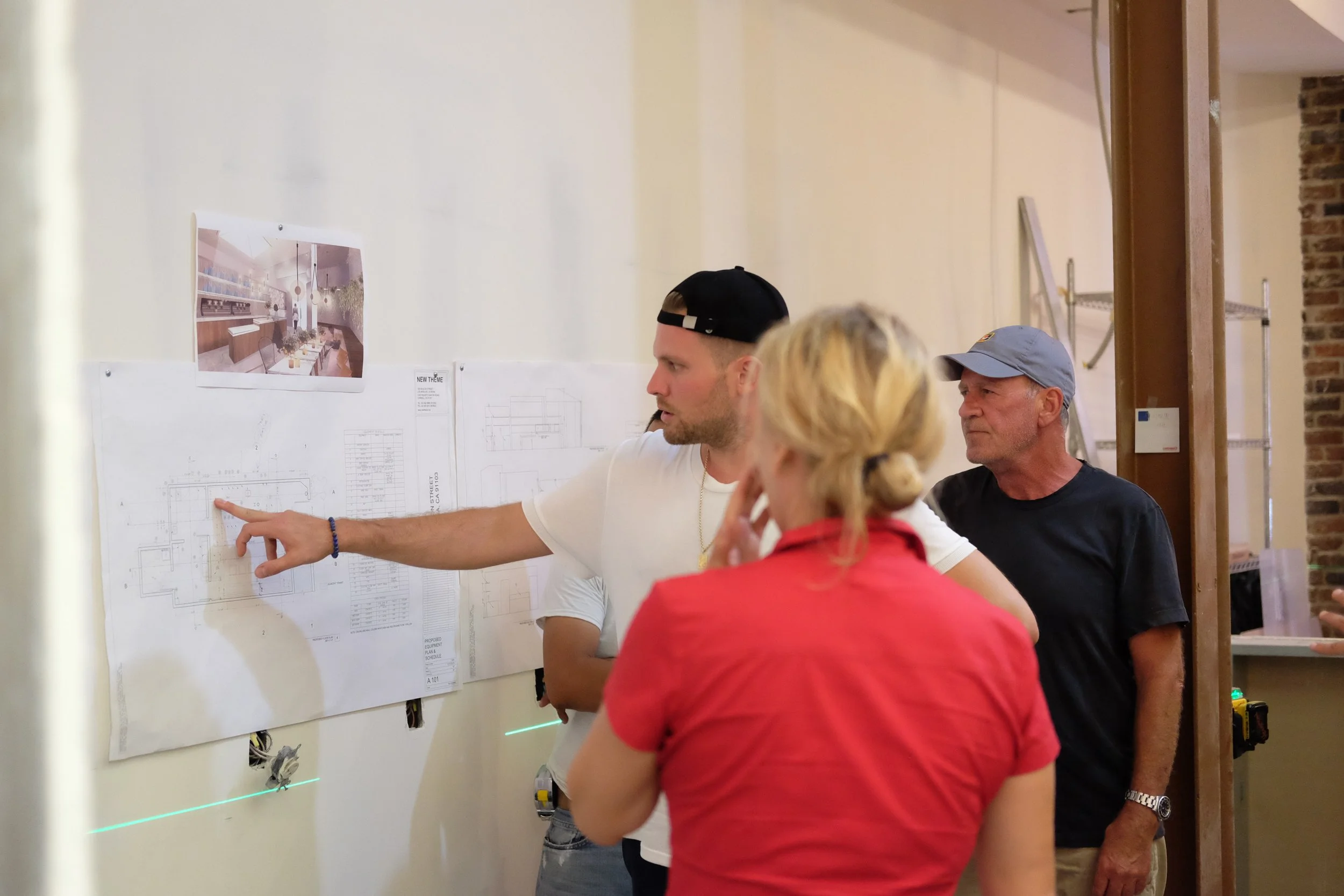 Three people discussing architectural blueprints on a wall, with a digital rendering of an interior space above the plans.